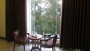 A room with a large window, two wooden chairs, a small round table, and a view of trees outside.