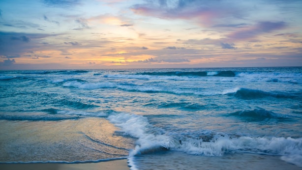 A beach with waves and a sunset.