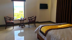 A hotel room with a bed, two chairs, a small table, a TV, and a window with blinds.