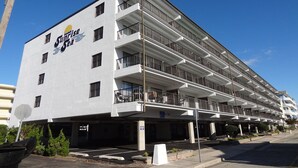 Un hôtel à plusieurs étages doté de balcons, avec un ciel dégagé et un espace de stationnement.
