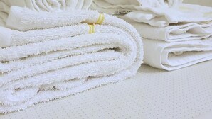 A stack of white towels with a yellow stripe, neatly folded on a white surface with a dotted pattern. - Blåtind Apartments (Fjord)
