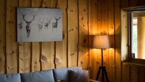 A cozy room with a wooden wall, a gray sofa, a floor lamp, and a painting of deer. - Blåtind Apartments (Fjord)