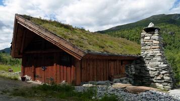 Une cabane en bois avec un toit recouvert d’herbe et une cheminée en pierre.