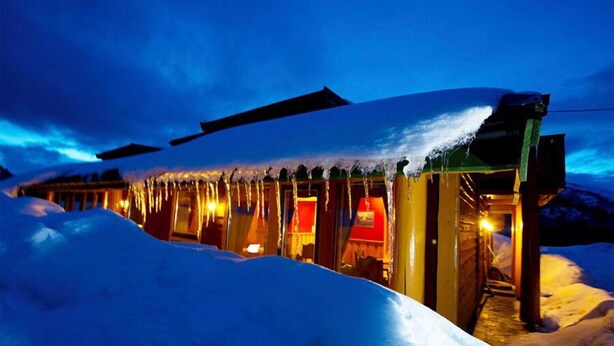 A snow-covered building with icicles hanging from the roof, illuminated by warm interior lights. - Blåtind Apartments (Fjord)
