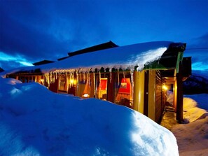 A snow-covered building with icicles hanging from the roof, illuminated by warm interior lights. - Blåtind Apartments (Fjord)