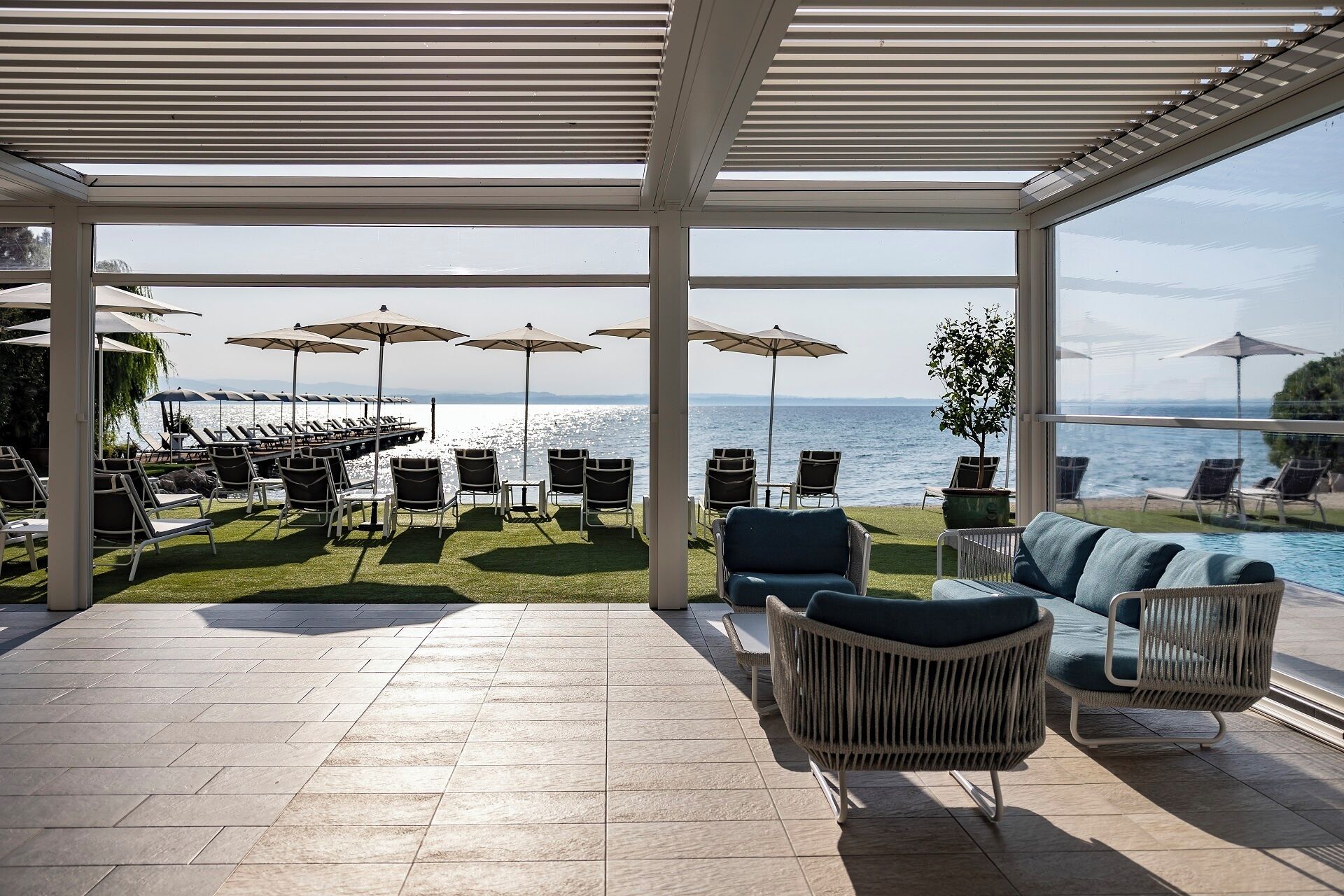 Un área de estar al aire libre con sillones reclinables y sombrillas, una piscina y vistas al mar.