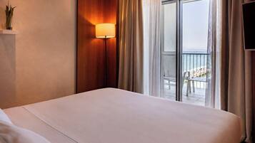 Habitación de hotel con cama, lámpara de pared, vista al balcón y televisión en la pared.