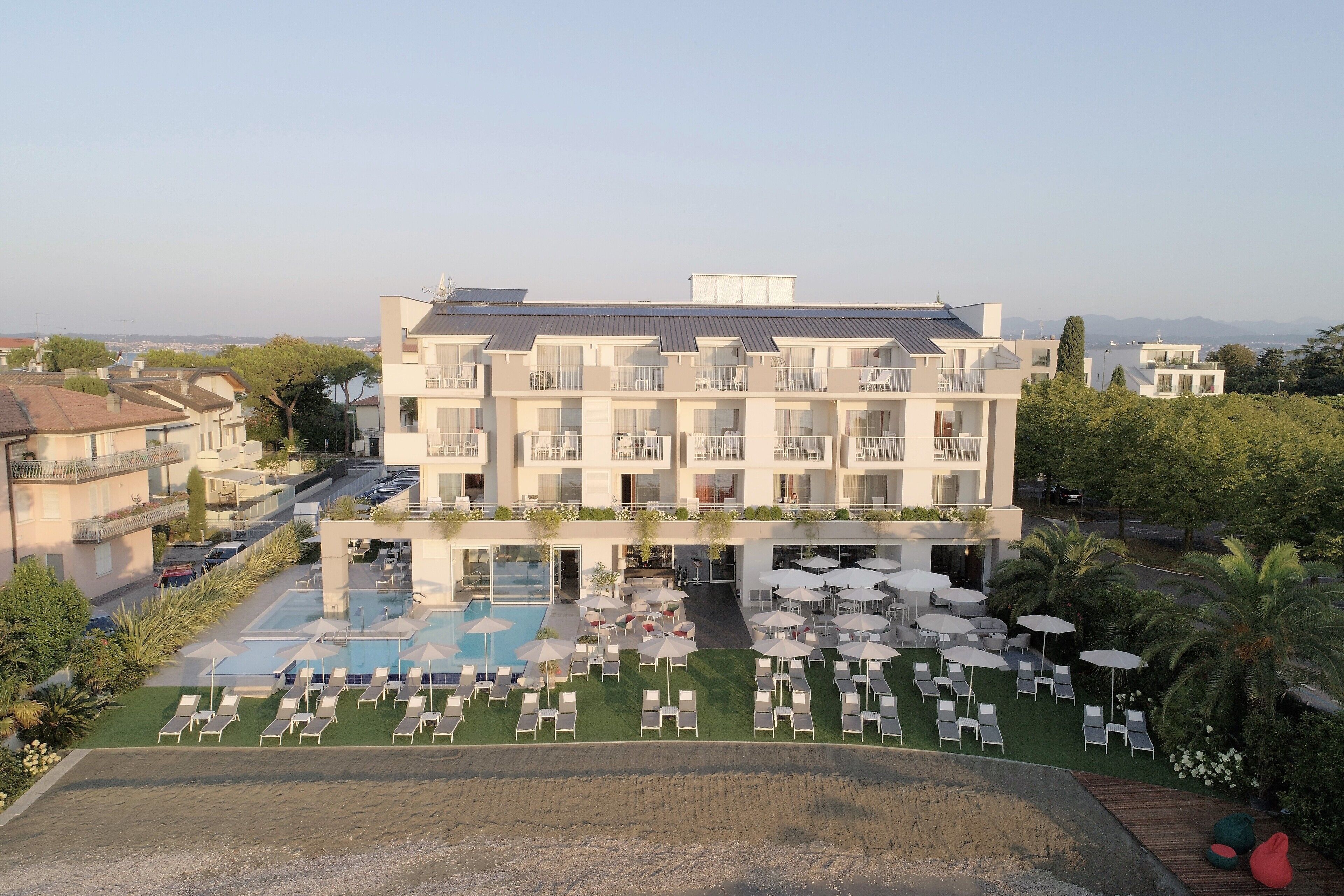 A modern hotel with a rooftop pool, multiple balconies, and a landscaped garden area.