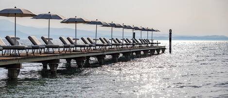 A pier with sun loungers and umbrellas, extending into a body of water.