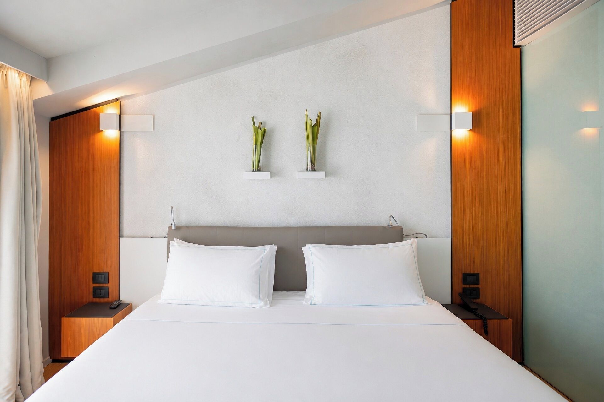 Ein Hotelzimmer mit einem großen Bett, zwei Nachttischen, einem Holzkopfende und Wandleuchten.