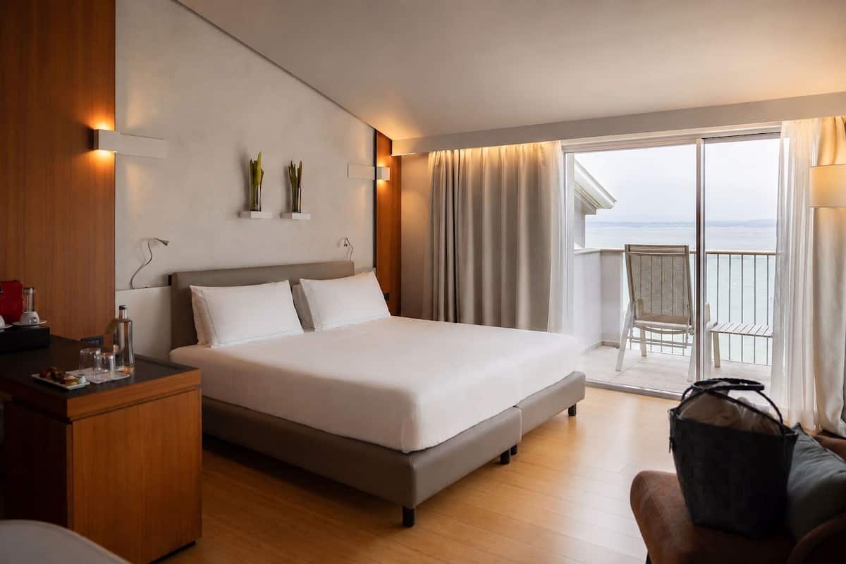 A hotel room with a bed, a desk, a chair, and a balcony with a view.