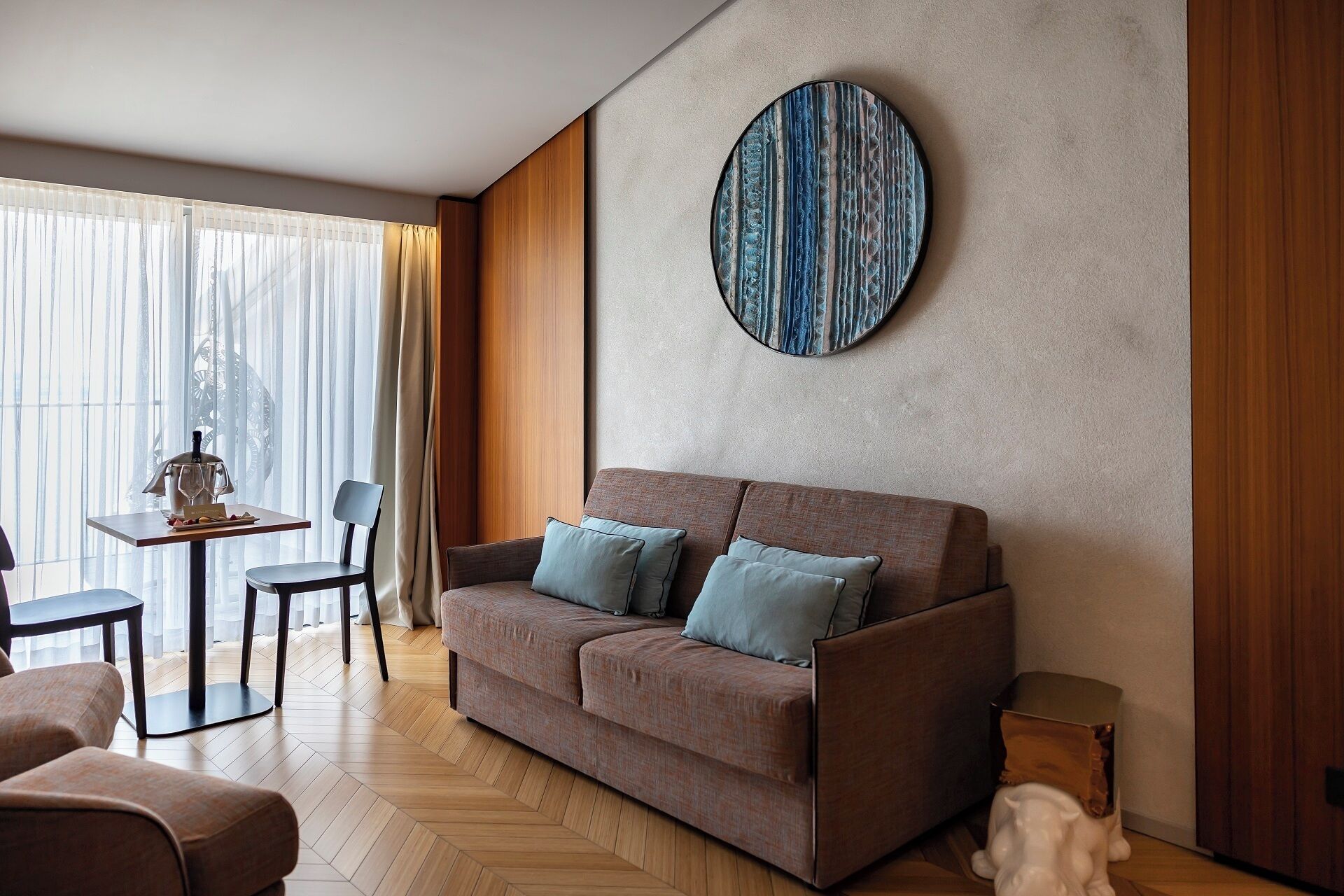 A modern living room with a sofa, a table with a wine bottle, and a decorative wall piece.
