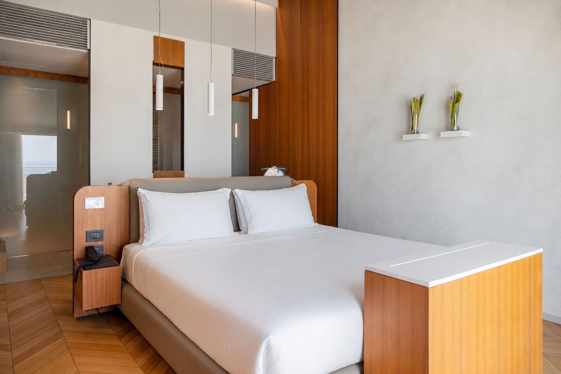 Una habitación de hotel moderna con una cama, mesita de noche, lámpara y una planta pequeña en la pared.