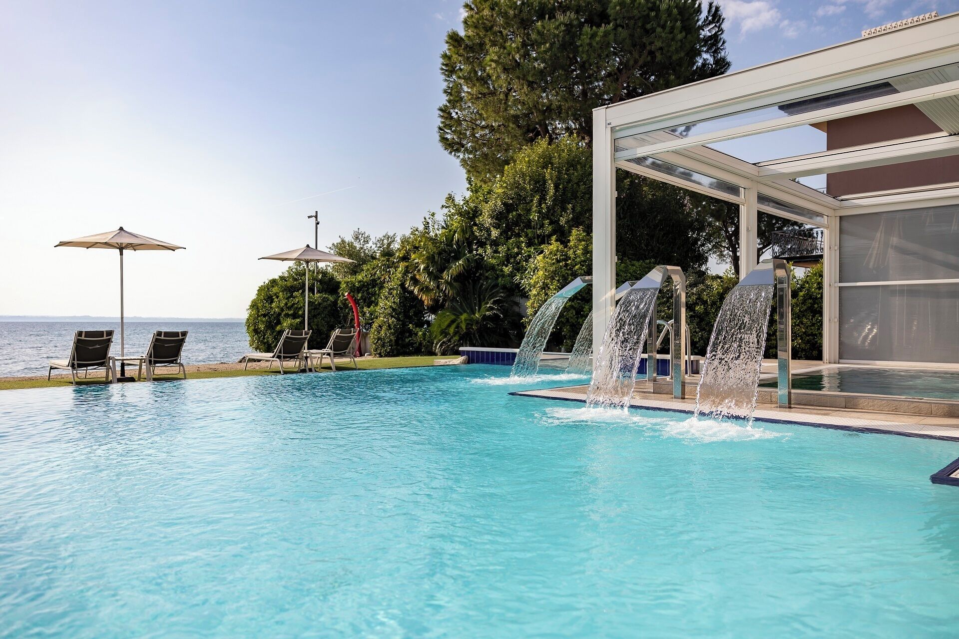 Una piscina con due lettini prendisole e un ombrellone, una fontana e un'area vetrata.