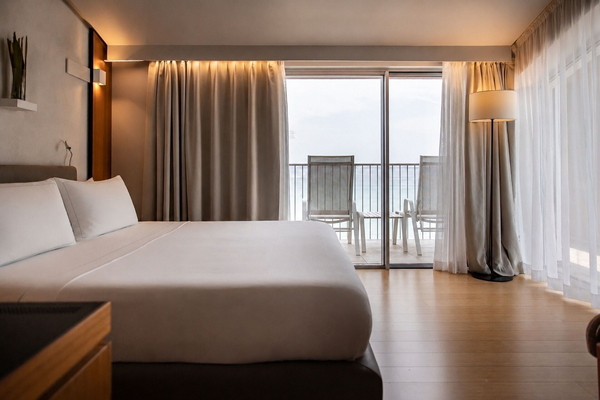 A hotel room with a large bed, a balcony with chairs, and a view of the sea.