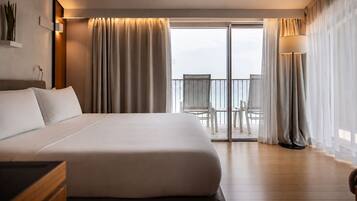A hotel room with a large bed, a balcony with chairs, and a view of the sea.