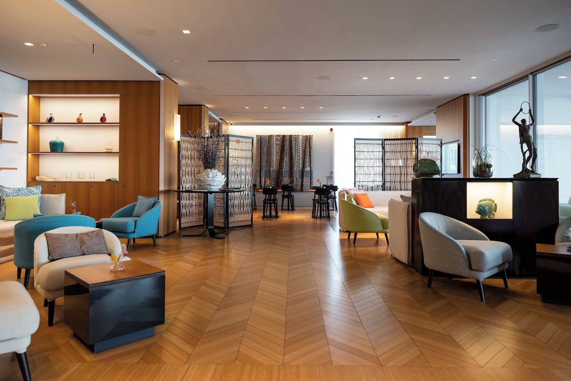 A spacious living area with a herringbone floor, modern furniture, and a view through large windows.