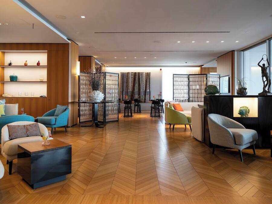 A spacious living area with a herringbone floor, modern furniture, and a view through large windows.