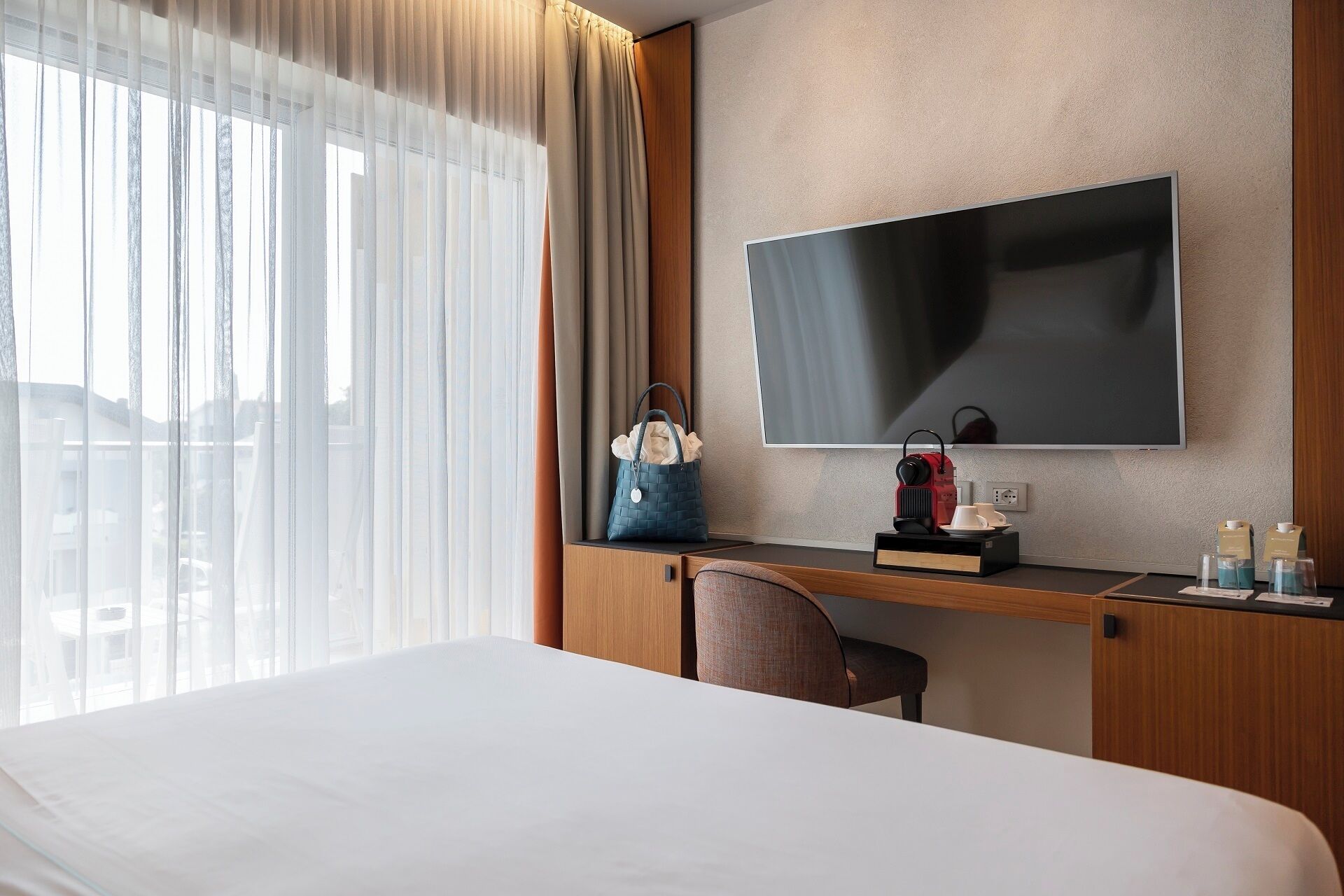 Habitación de hotel con cama, escritorio con televisor, una silla, un bolso y cafetera.