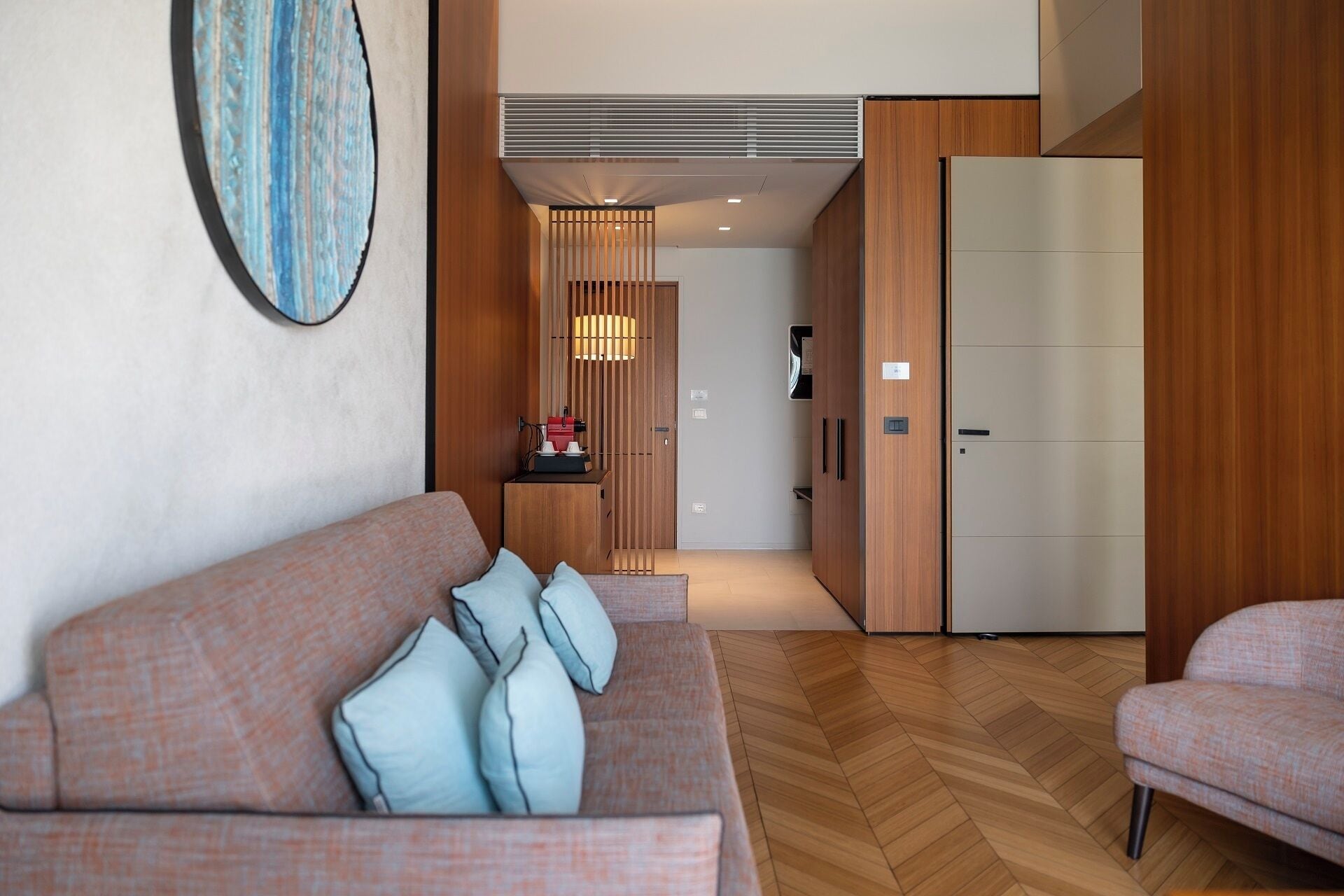 A modern hotel room with a sofa, a dining area, and a wardrobe.