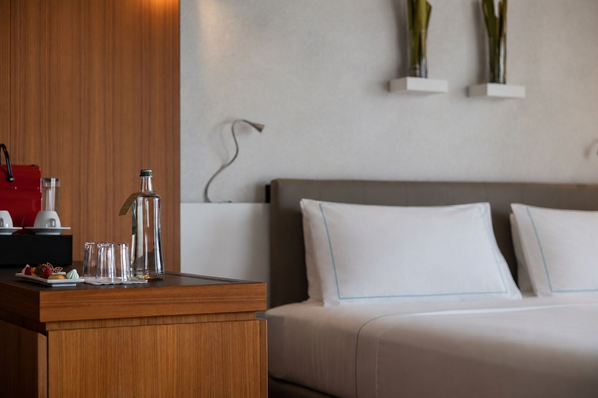 A hotel room with a wooden desk, a bed with white bedding, and two wall-mounted vases.