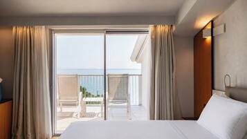 A hotel room with a large bed, a balcony with chairs, and a view of the sea.