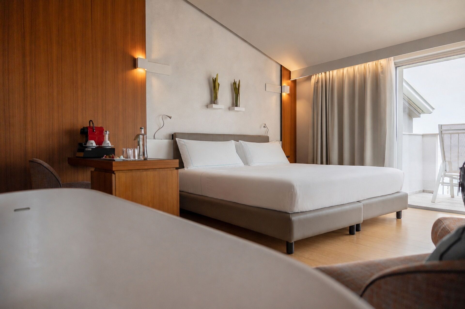 A modern hotel room with a bed, bedside table, and a view of the balcony.