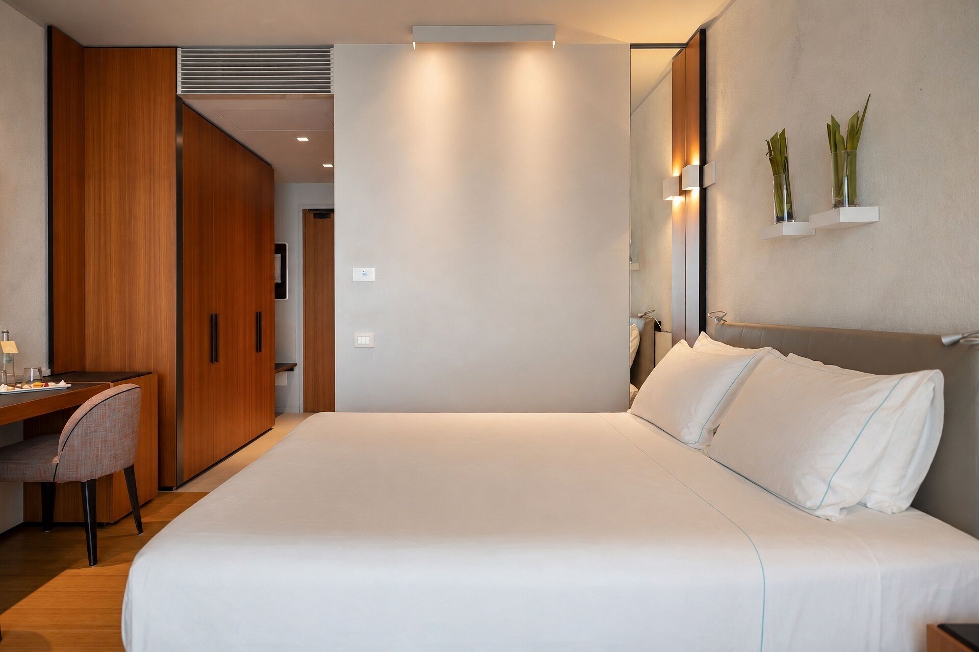 A modern hotel room with a large bed, a desk, and a wardrobe.