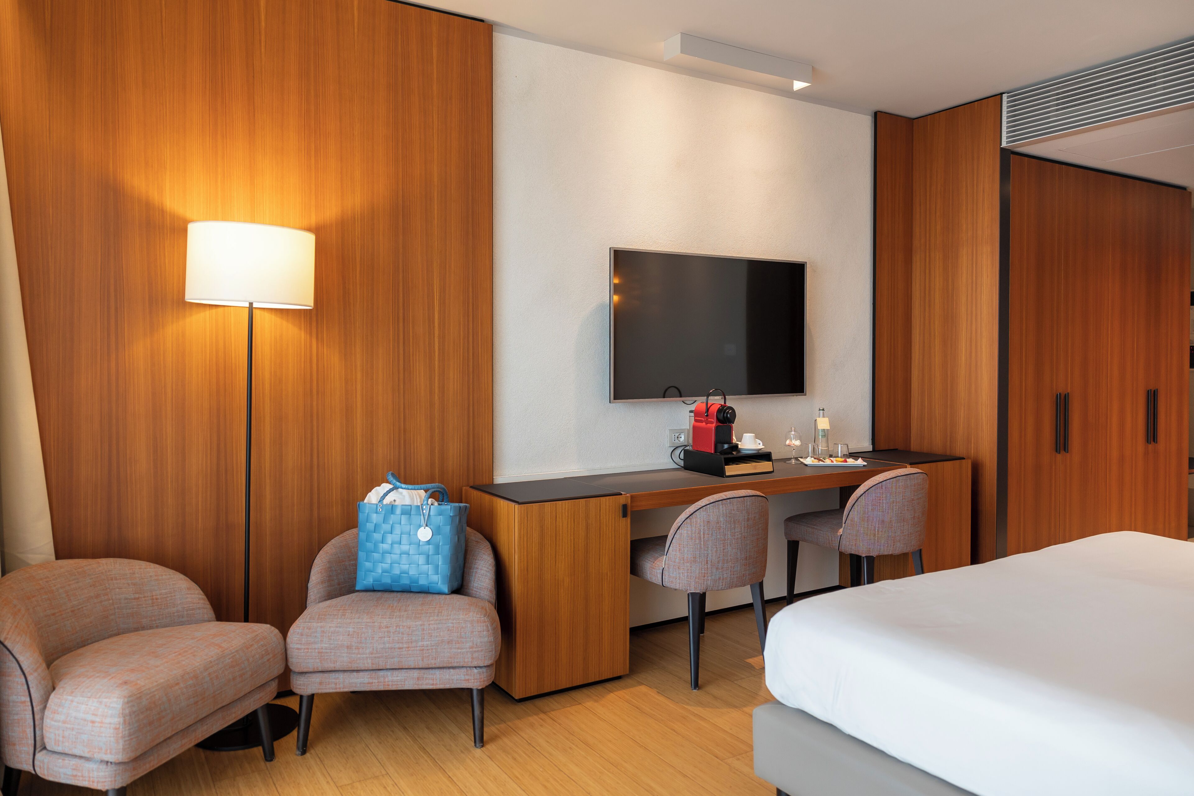 Habitación de hotel con cama, dos sillones, escritorio con televisor de pantalla plana, lámpara y minibar.