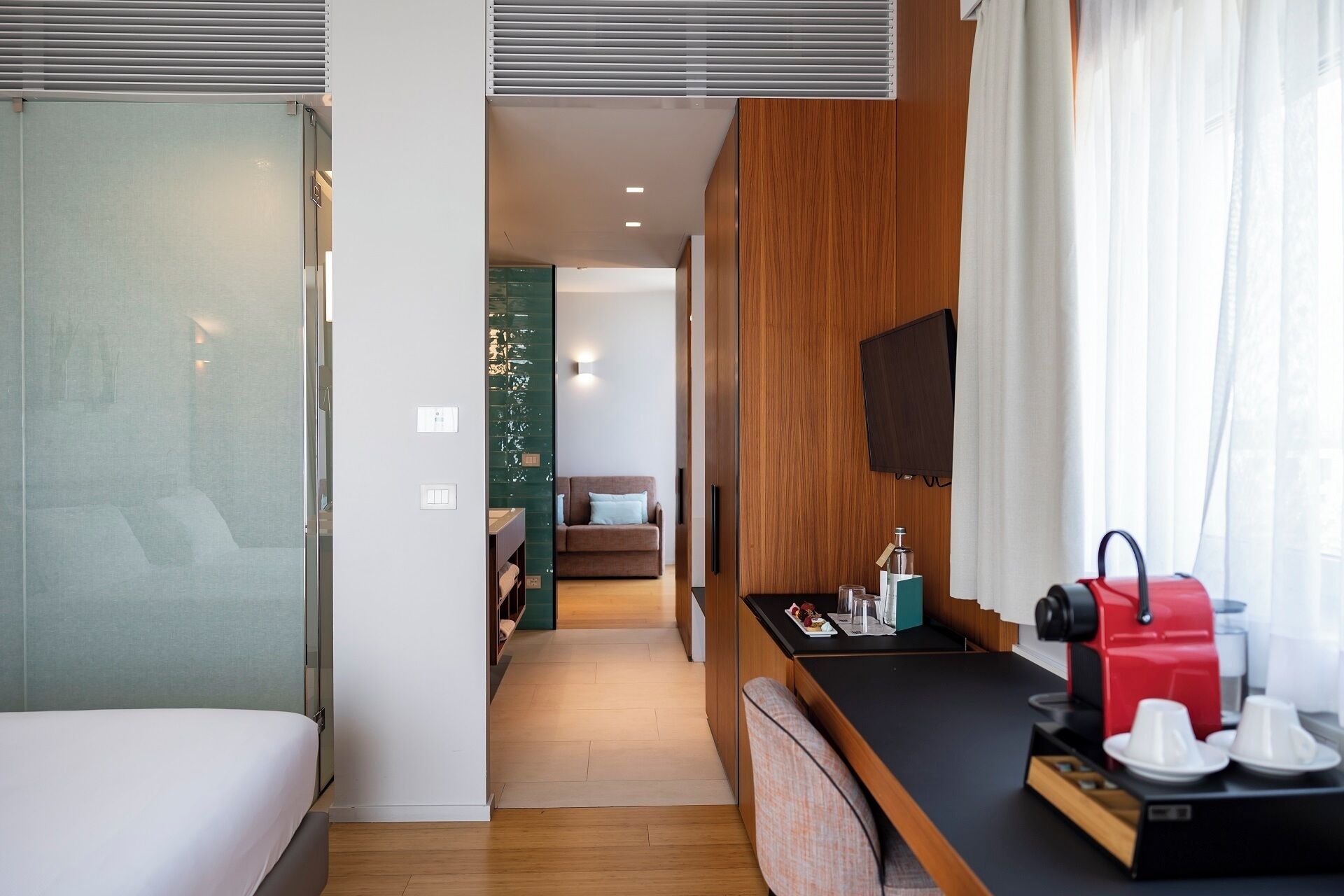 A hotel room with a bed, a kitchenette, a TV, and a window with curtains.