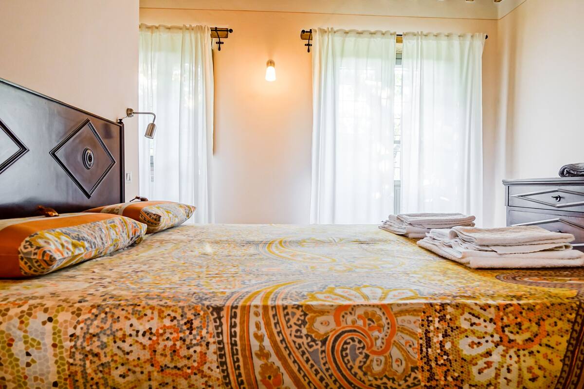 Una habitación de hotel con cama, cortinas, lámpara de noche, cómoda y ventana.
