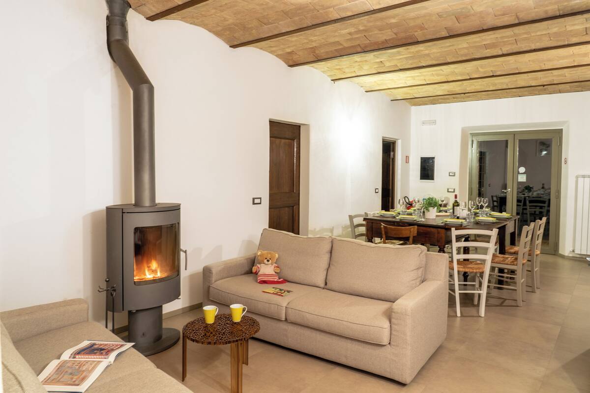 Una sala de estar acogedora con una estufa de leña, un sofá, una mesa de comedor con sillas y un osito de peluche.