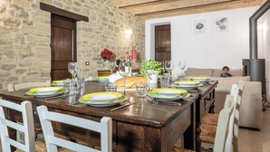 Un espace repas agrémenté d’un mur en pierre rustique, de poutres en bois au plafond et d’une longue table à manger dressée pour le repas.