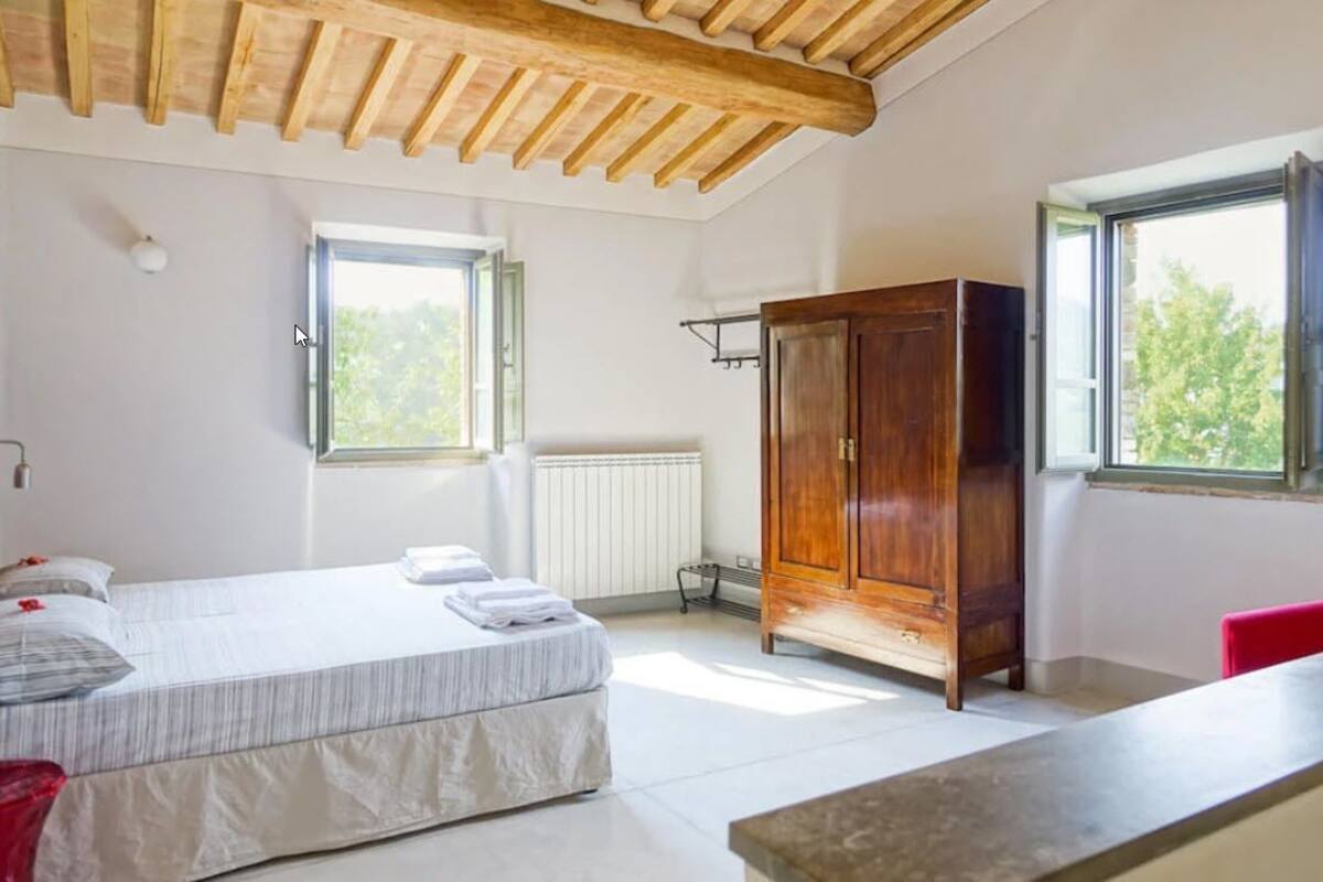 Un dormitorio con cama, armario de madera, radiador y ventana.