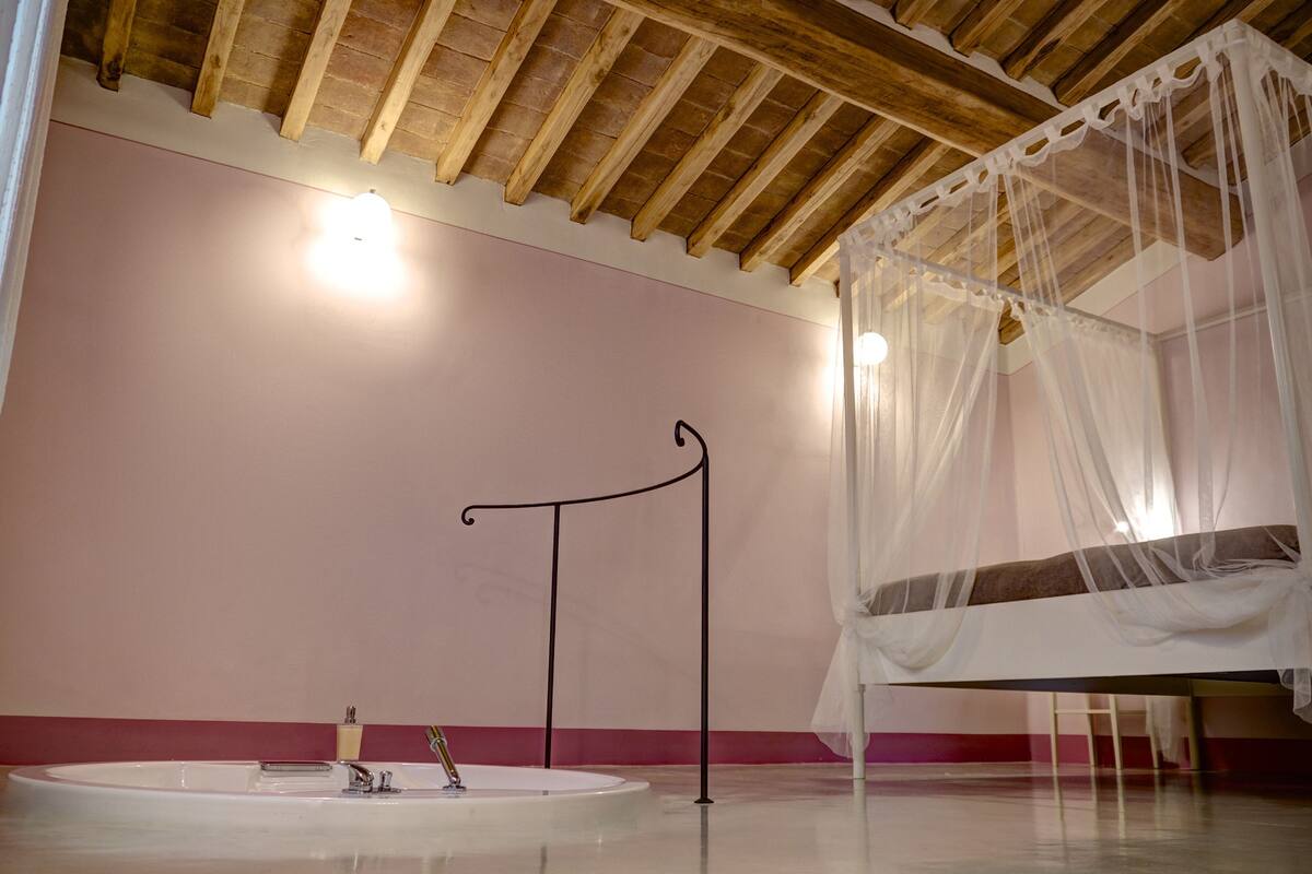 Una habitación con una cama bajo un dosel, una mesa redonda blanca y una lámpara fijada a la pared.