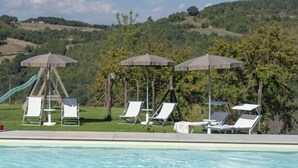 Une piscine entourée de verdure et de collines, avec des chaises longues et des parasols.
