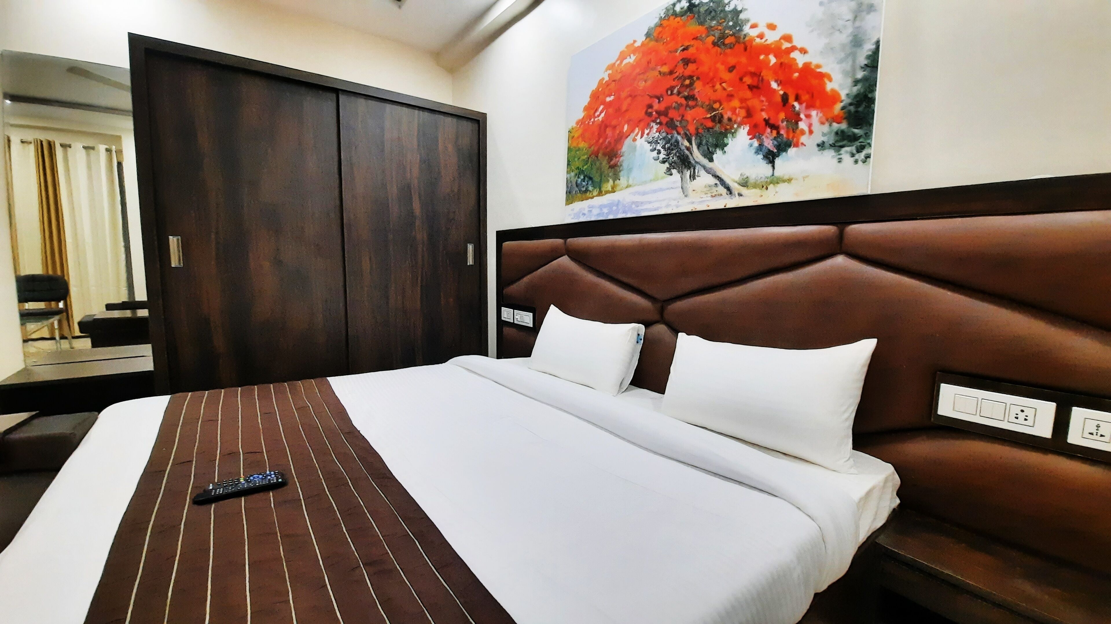 A hotel room with a large bed, a brown headboard, a painting of a tree, and a wardrobe.