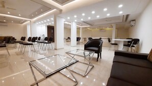 A spacious lobby with a modern design, featuring a glass coffee table, a black leather sofa, and several chairs arranged for seating. - Hotel Sai Village Gurgaon (Gurugram)