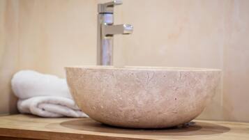 Un bagno con un lavandino in pietra beige, un piano in legno e un asciugamano bianco.