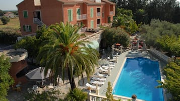 Un hotel con piscina, mobiliario exterior y abundante vegetación.