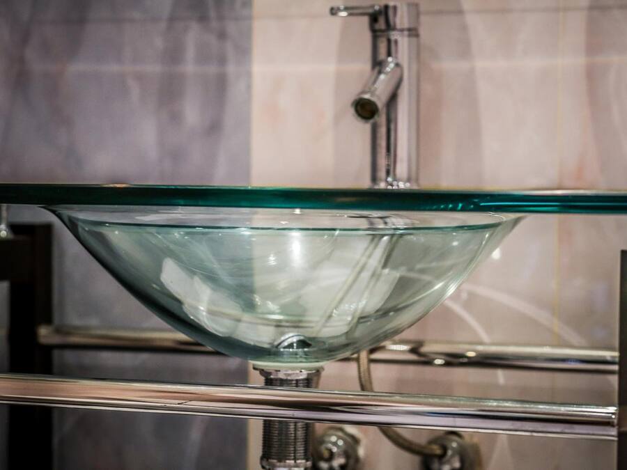 A clear glass bowl sink with a metallic faucet and a chrome frame.