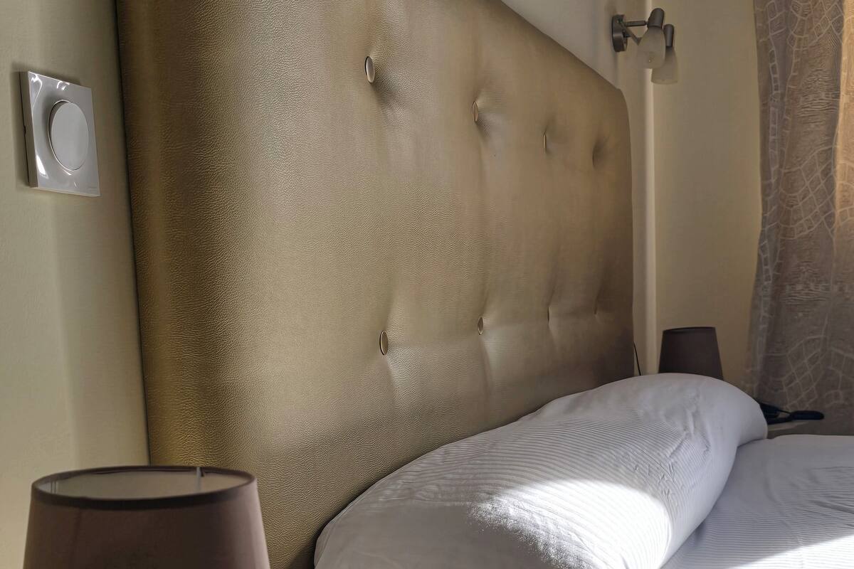 Une chambre d’hôtel avec une tête de lit capitonnée, une table de chevet avec une lampe et un lit recouvert de draps blancs.