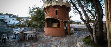 Un patio de piedra con una estructura de torre de ladrillo rústica, mobiliario exterior y un sendero de piedra.