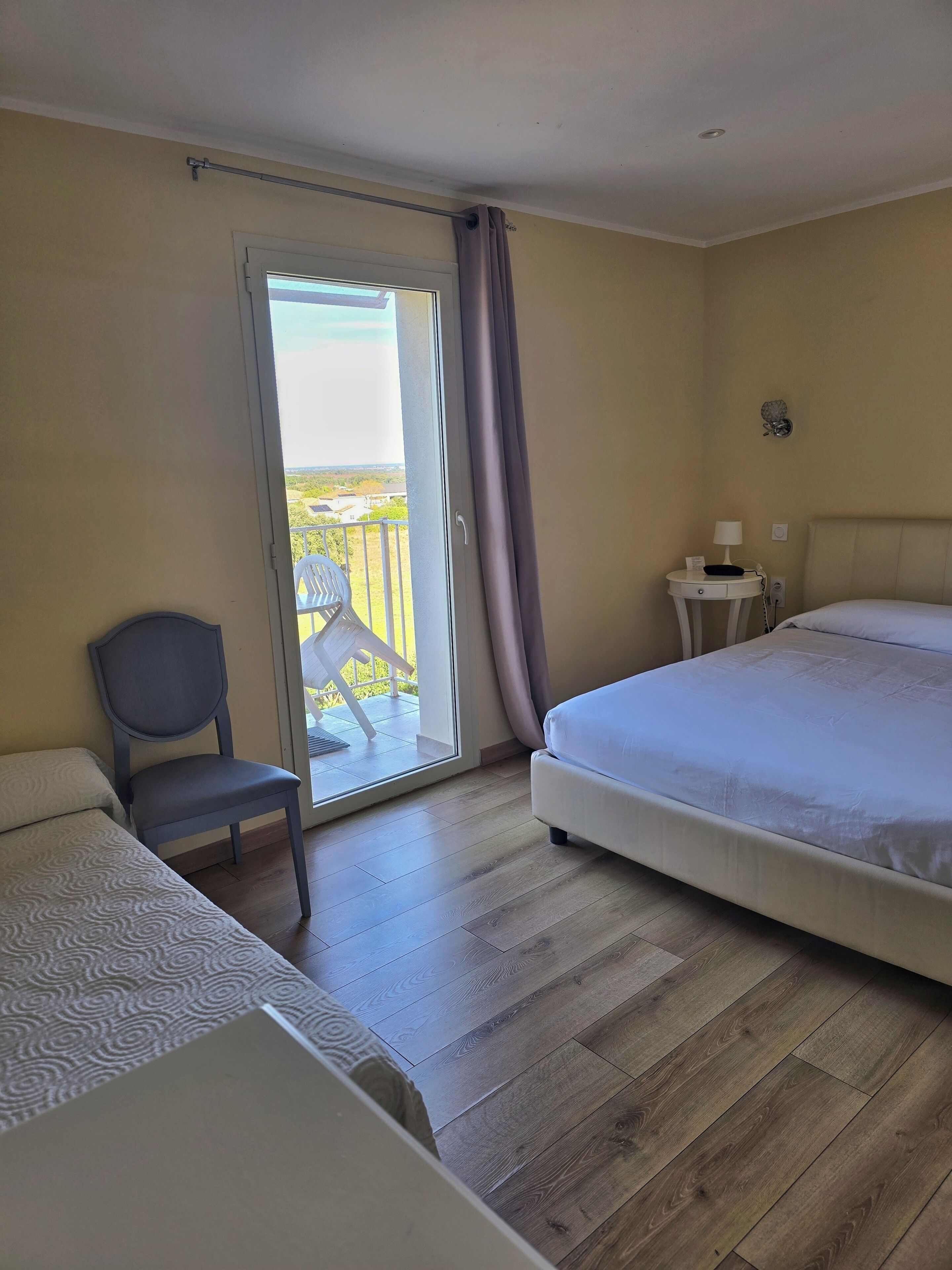 A hotel room with a bed, a chair, a small table with a lamp, and a view of the outdoors through a sliding door.