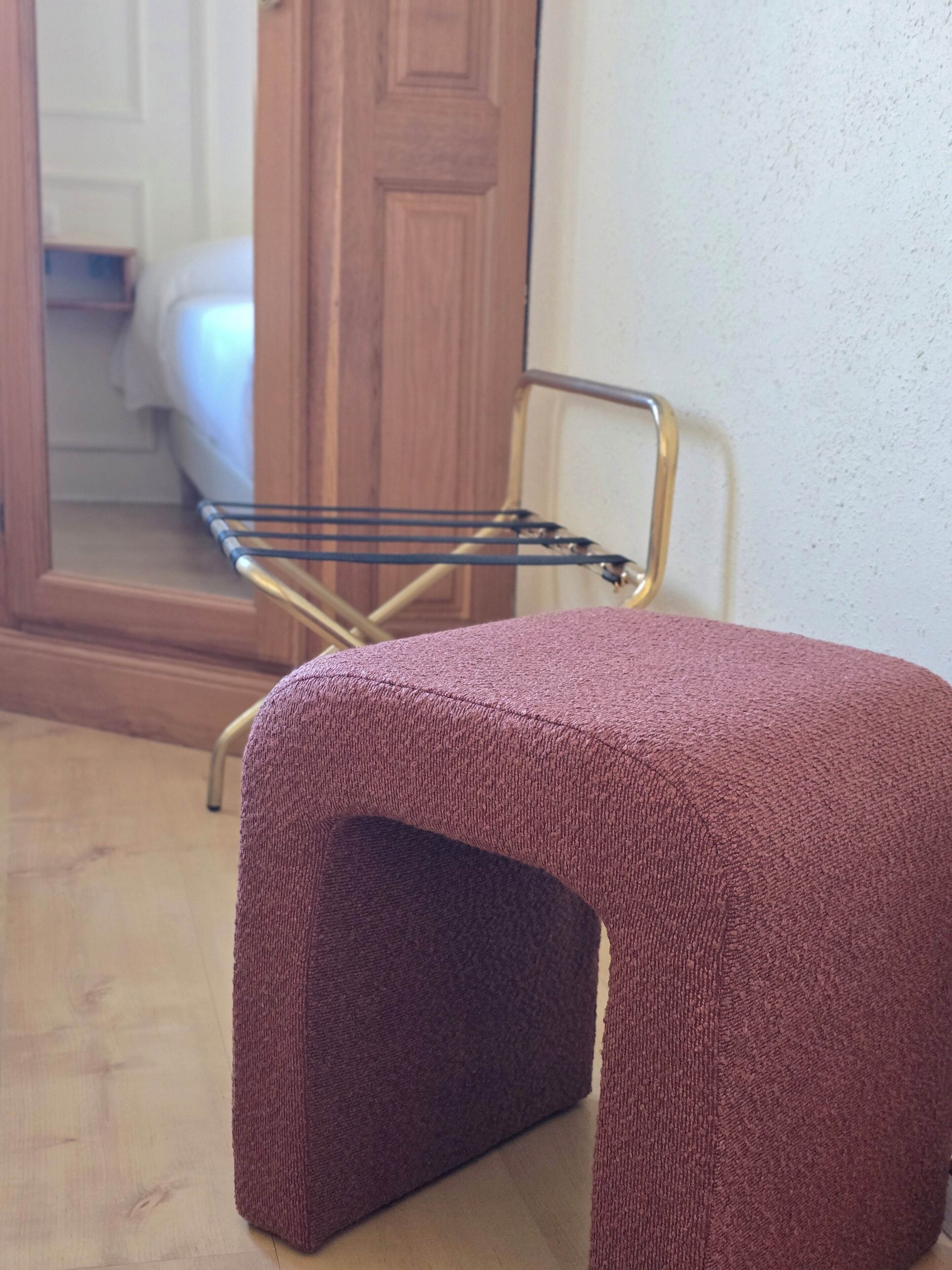 Un petit tabouret carré, de couleur violette et à la texture particulière, doté d’une structure métallique, posé sur un plancher en bois.