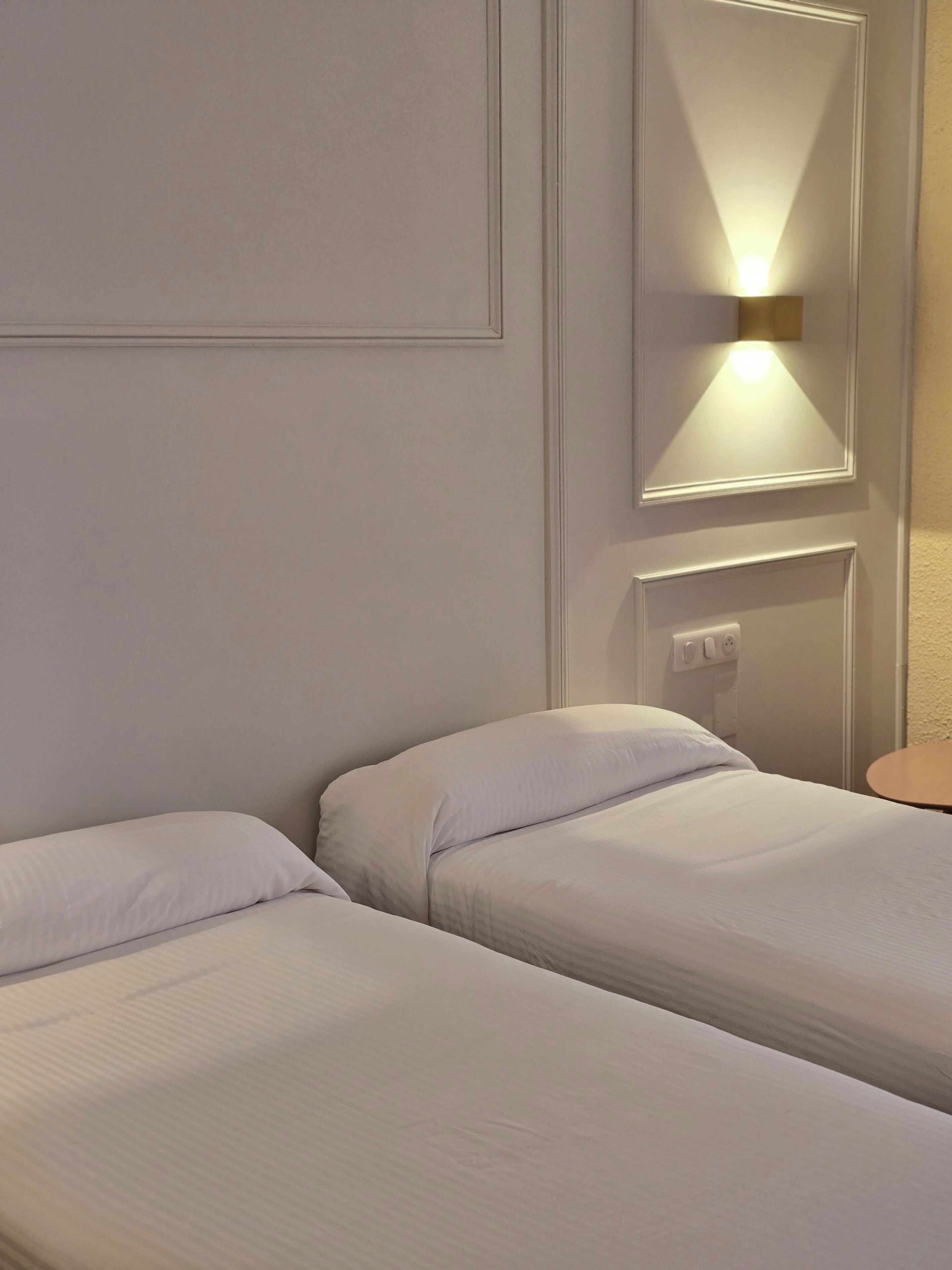 Ein Hotelzimmer mit zwei Einzelbetten, einem Nachttisch, einer Wandlampe und einer Steckdose.