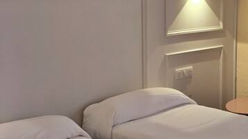 Ein Hotelzimmer mit zwei Einzelbetten, einem Nachttisch, einer Wandlampe und einer Steckdose.