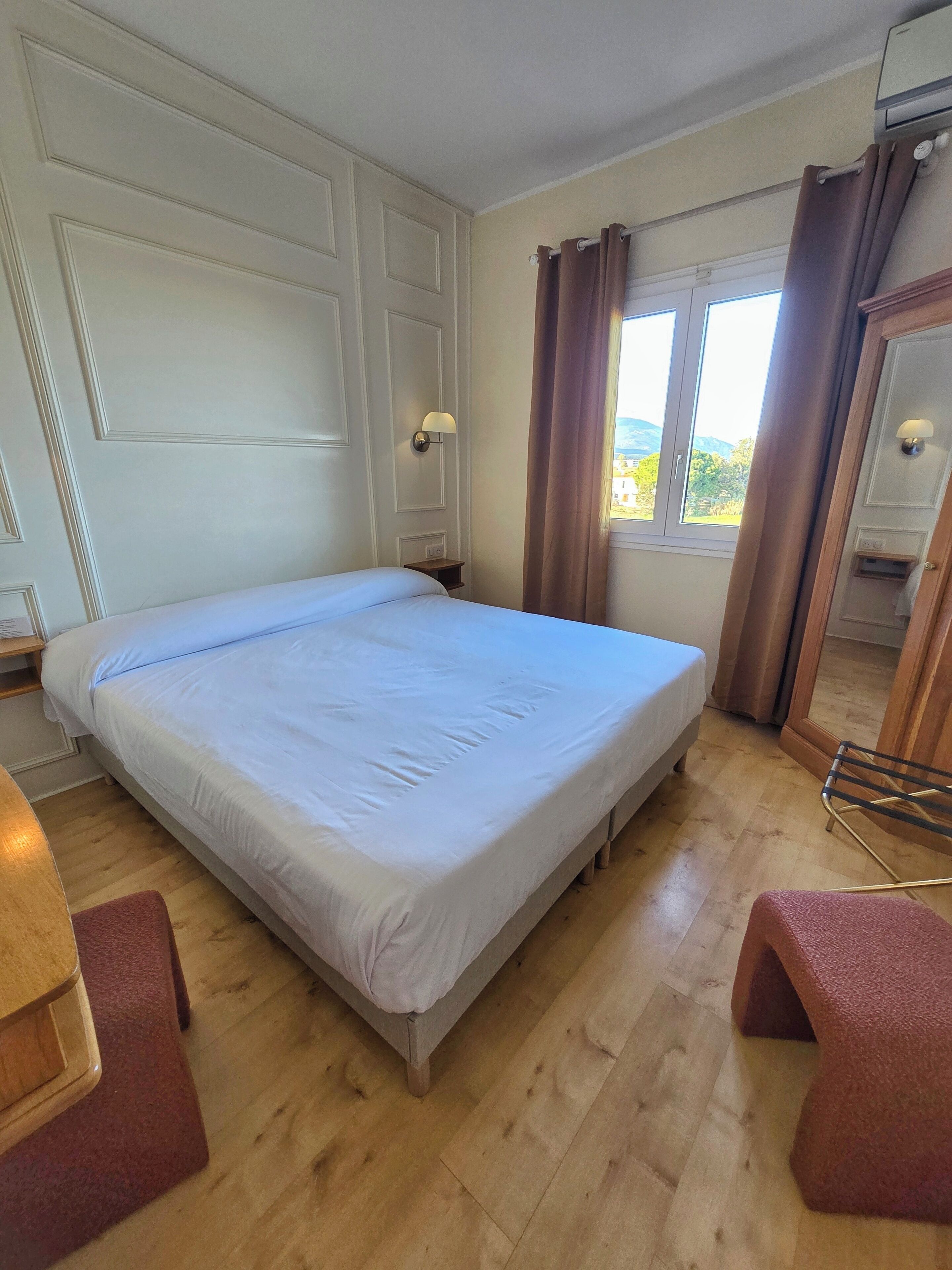 Une chambre d’hôtel avec un grand lit, un plancher en bois, une fenêtre avec des rideaux et un miroir muni d’un porte-serviettes.