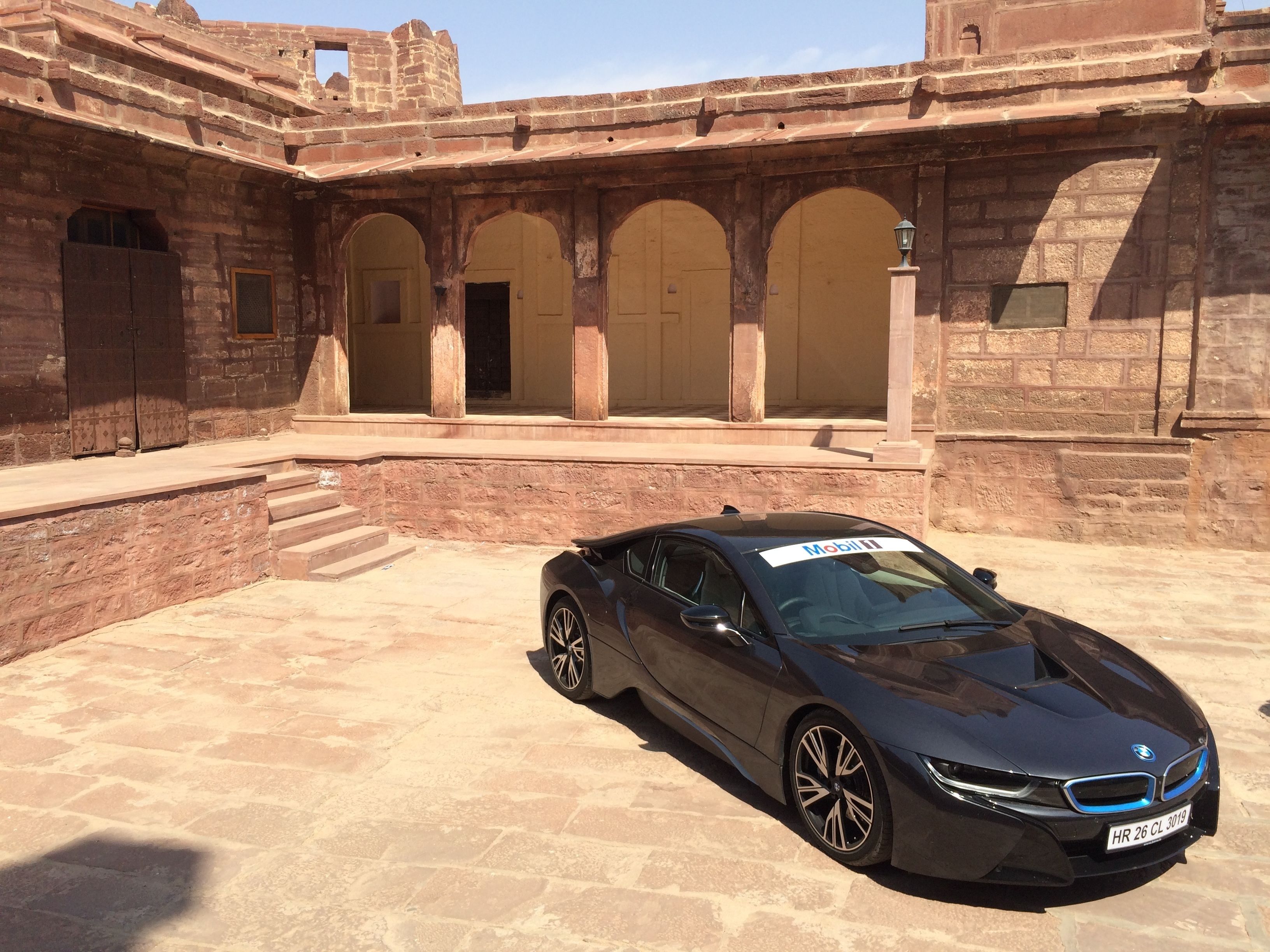 A BMW i8 parked in front of a historic building with arched doorways and stone walls.