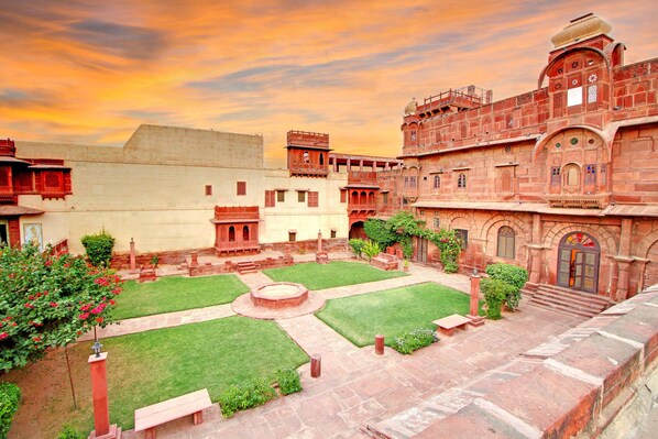 A courtyard with a central fountain, surrounded by traditional architecture and a clear sky.